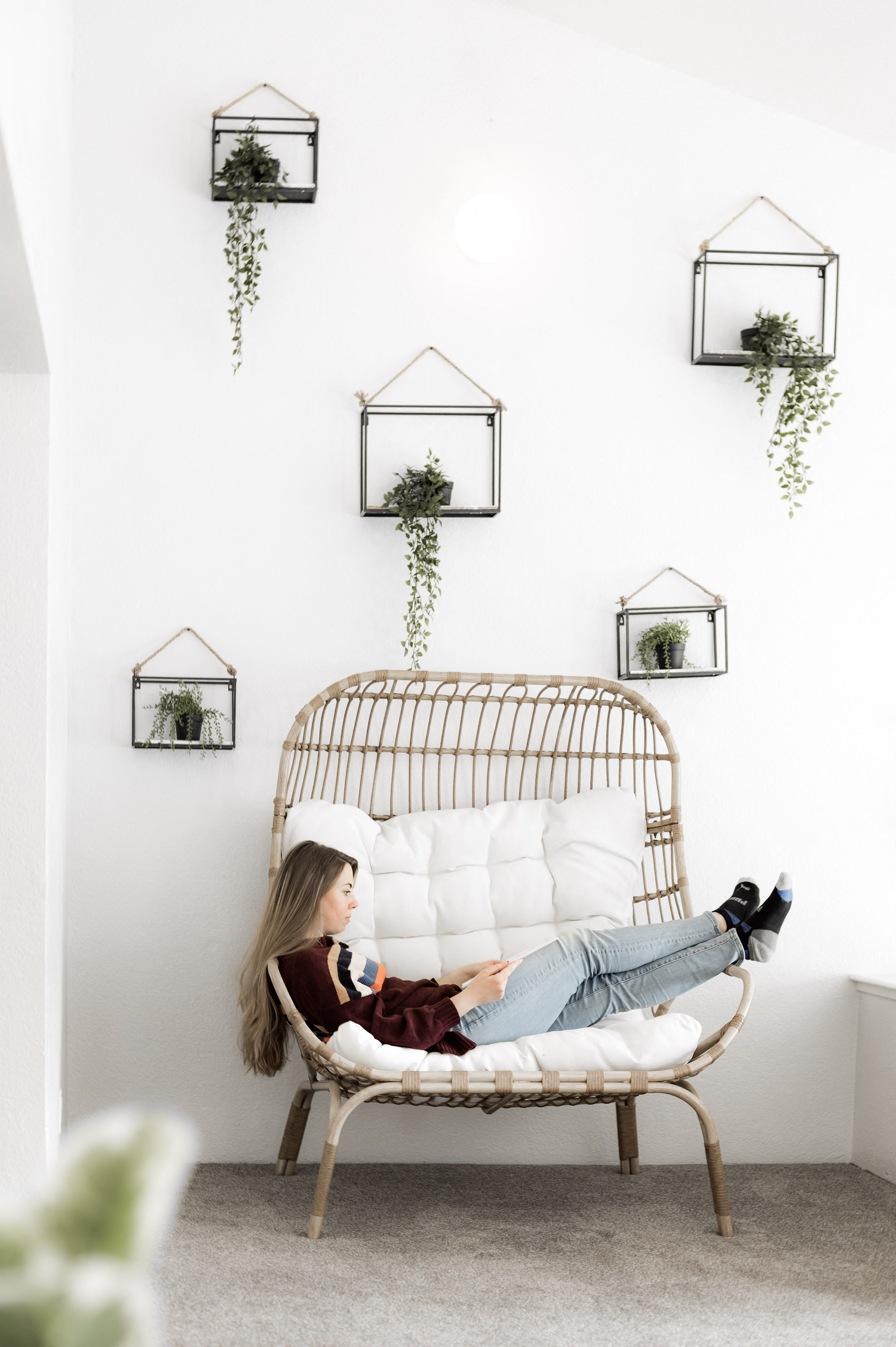 Young woman lounging in oversized chair in front of wall with hanging plants